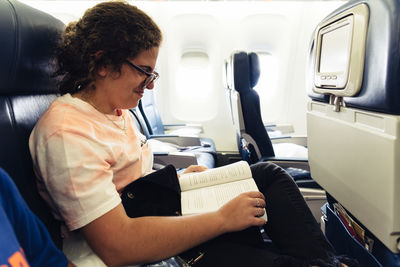 Smiling woman reading book while sitting in airplane