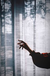 Cropped hand of woman reaching curtain at home