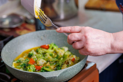 Female hands adds a scrambled egg yolks to frying vegetables while cooking omelette