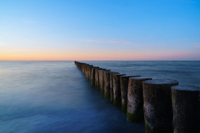 Wooden posts in sea against sky during sunset