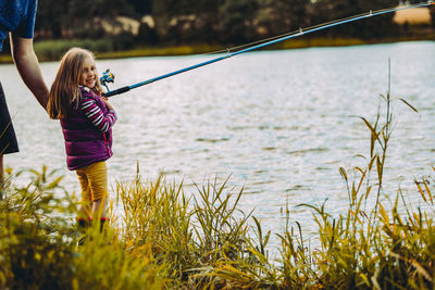 Smiling girl by father fishing in lake