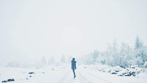 Rear view of woman jumping on snow covered landscape