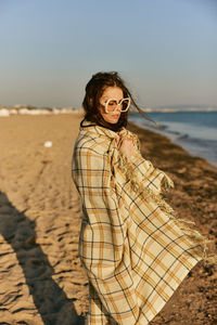 Young woman standing at beach against sky