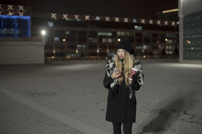 Full length of woman standing in illuminated city at night