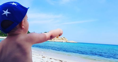 Shirtless baby boy pointing at sea against sky