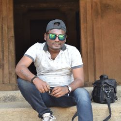 Portrait of young man in sunglasses sitting at entrance