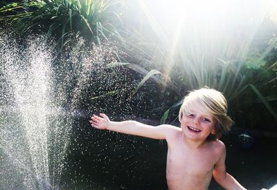 Portrait of cute boy playing with spraying water against plants