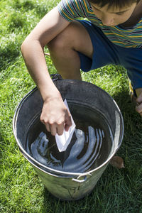 High angle view of boy holding paper boat on water in bucket