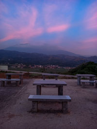 Empty bench and tables against sky during sunset