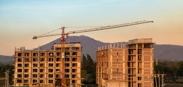 Cranes at construction site in city against sky.