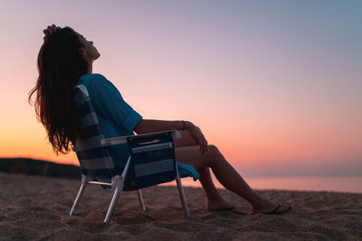 Side view of woman sitting on chair at sunset