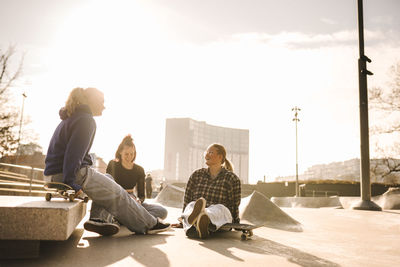 Teenage girls with skateboards sitting in skatepark