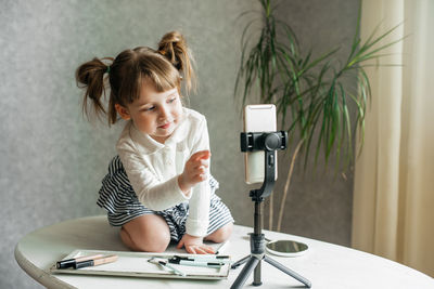 Full length of woman photographing while sitting on table