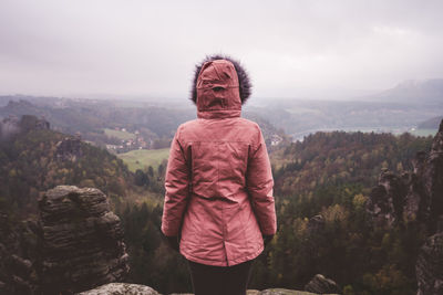 Rear view of woman standing on cliff against landscape