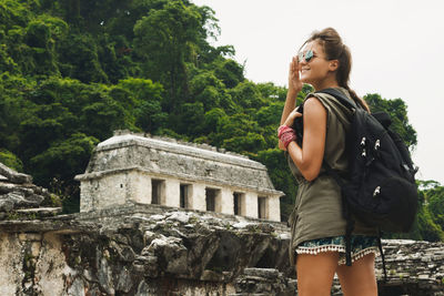 Low angle view of young woman standing against trees