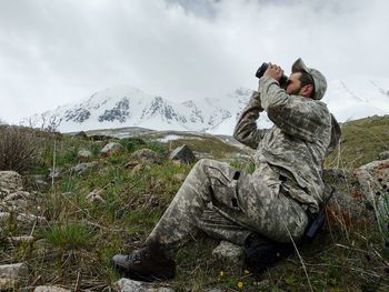 Man photographing on mountain against sky during winter