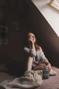 Young woman looking through the window while sitting at home