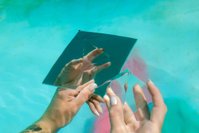 Cropped hand of woman holding pyramid crystal and mirror in swimming pool