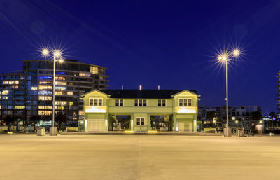 Illuminated street light by building against sky at night