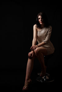 Portrait of woman sitting against black background