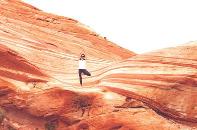 Woman exercising on rock formation against clear sky