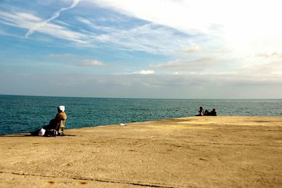 People sitting by sea against sky