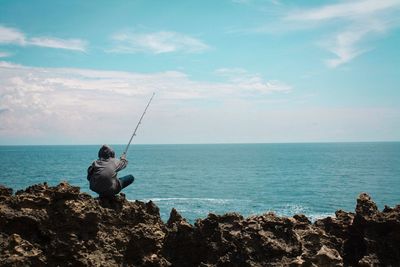 Man fishing in sea against sky