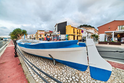 Boats moored on street by buildings against sky