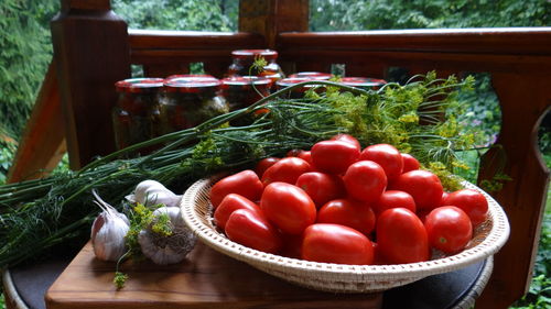 Close-up of tomatoes in bowl by jars and herbs on table