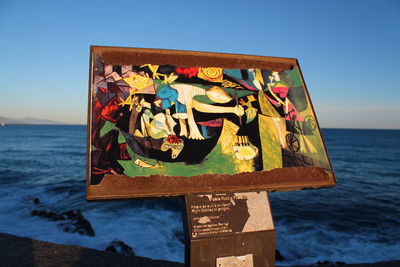 Graffiti on wall by sea against clear sky