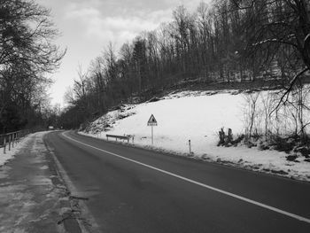 Road by trees against sky during winter