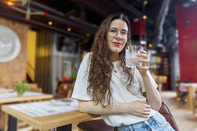 Portrait of young woman drinking water at cafe