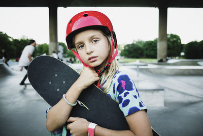 Portrait of girl wearing red helmet holding skateboard at park