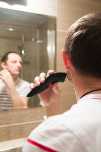 Young man trimming beard in bathroom