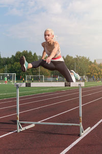 Full length of young woman exercising on field against sky