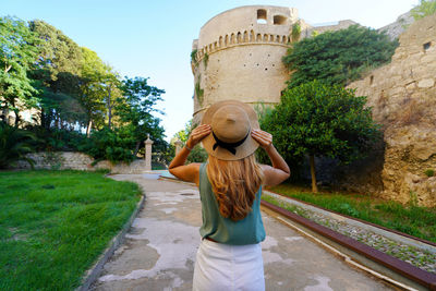 Back view of beautiful woman in crotone with charles v aragon castle in crotone, calabria, italy.