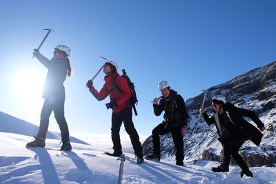 Young playful friends walking with ski poles on snowcapped mountain against sky