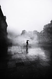 Silhouette people walking on wet street amidst buildings against sky during rainy season