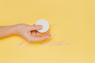 Cropped hand of woman holding thermometer against yellow background