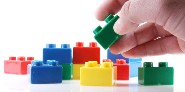 Cropped image of person arranging plastic blocks against white background