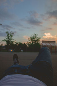 Low section of man resting against sky during sunset