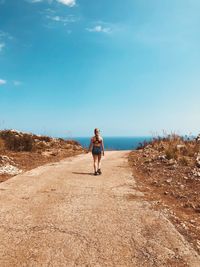 Rear view of teenage girl walking on footpath against blue sky