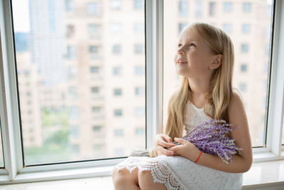 Girl with flowers looking up sitting at window sill