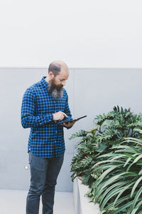 Busy male worker standing in creative workspace with plants and browsing tablet while working on new project