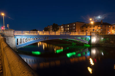 Illuminated bridge over river by buildings against sky at night