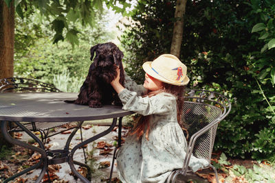 Rear view of girl playing with black little dog by plants