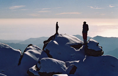 People standing by frozen lake against sky during winter