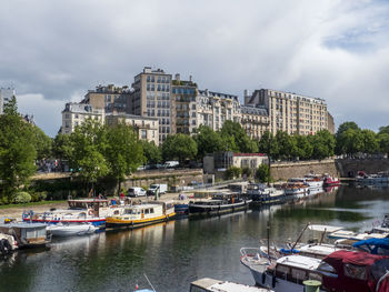 Boats moored at harbor by buildings against sky