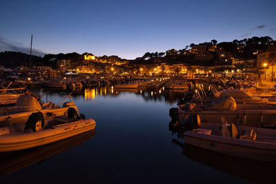 Boats on river amidst illuminated buildings in city at night