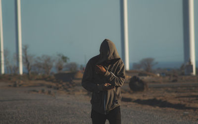 Man wearing hooded shirt walking on road against clear sky